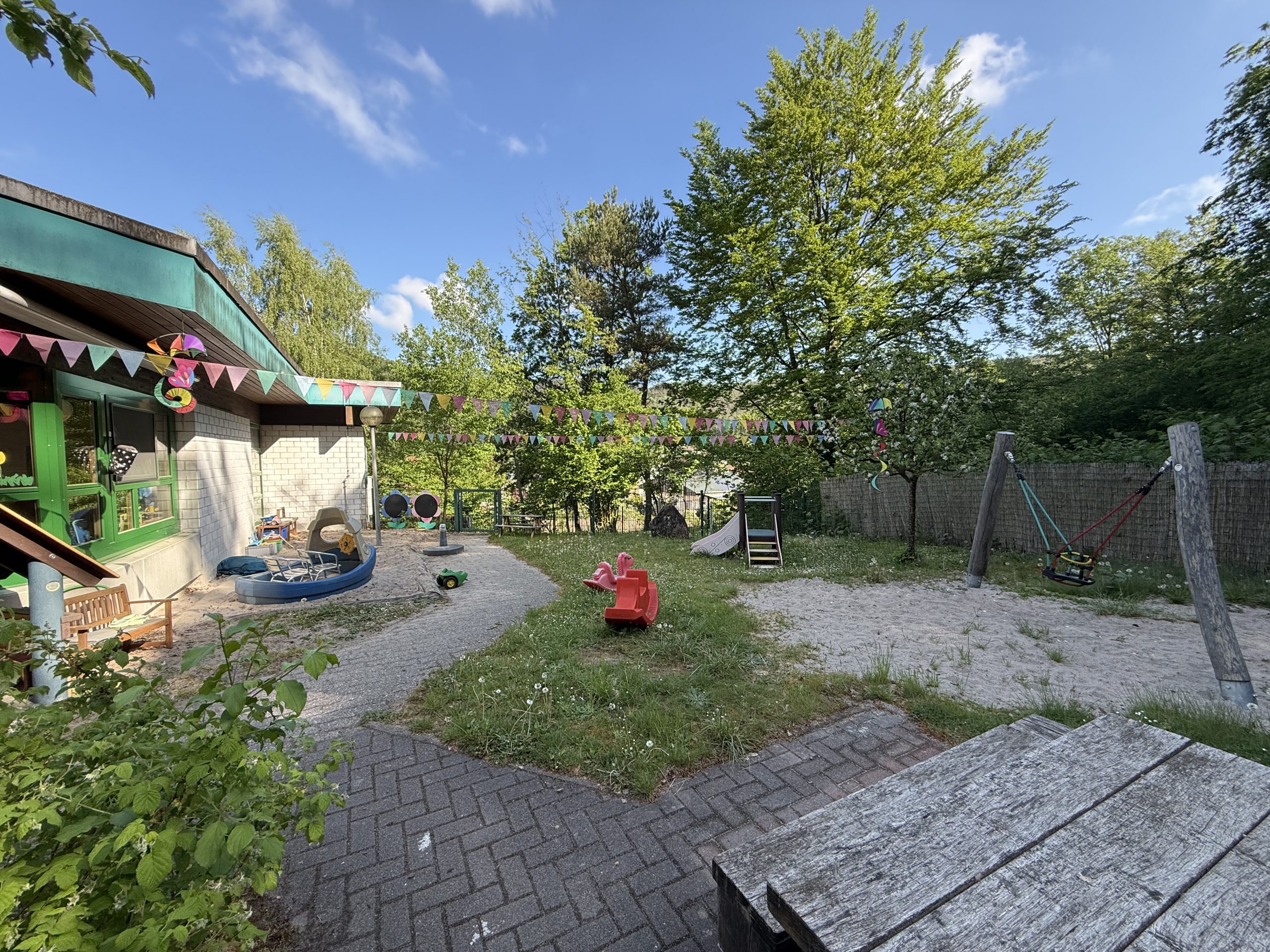 Der Außenbereich der blauen Gruppe, mit Sandkasten, kleiner Rutsche, Schaukel und Gartentisch