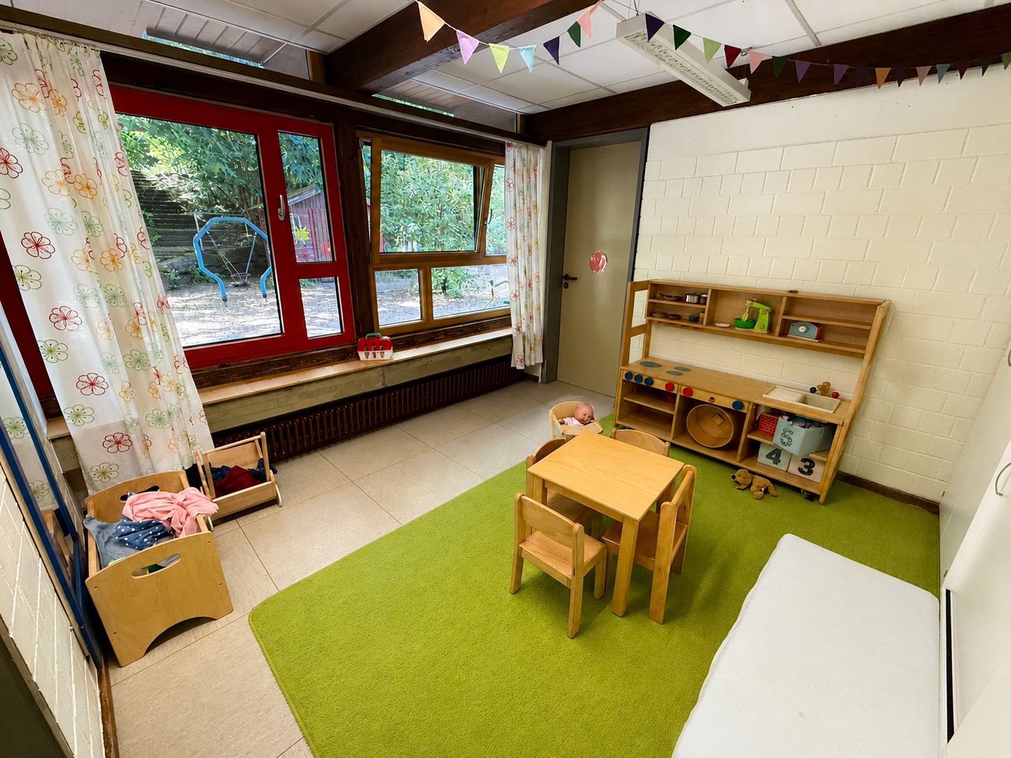 Zwischenraum der grünen Gruppe, mit einer Puppenküche, einem Tisch mit Stühlen und einem Puppenbett