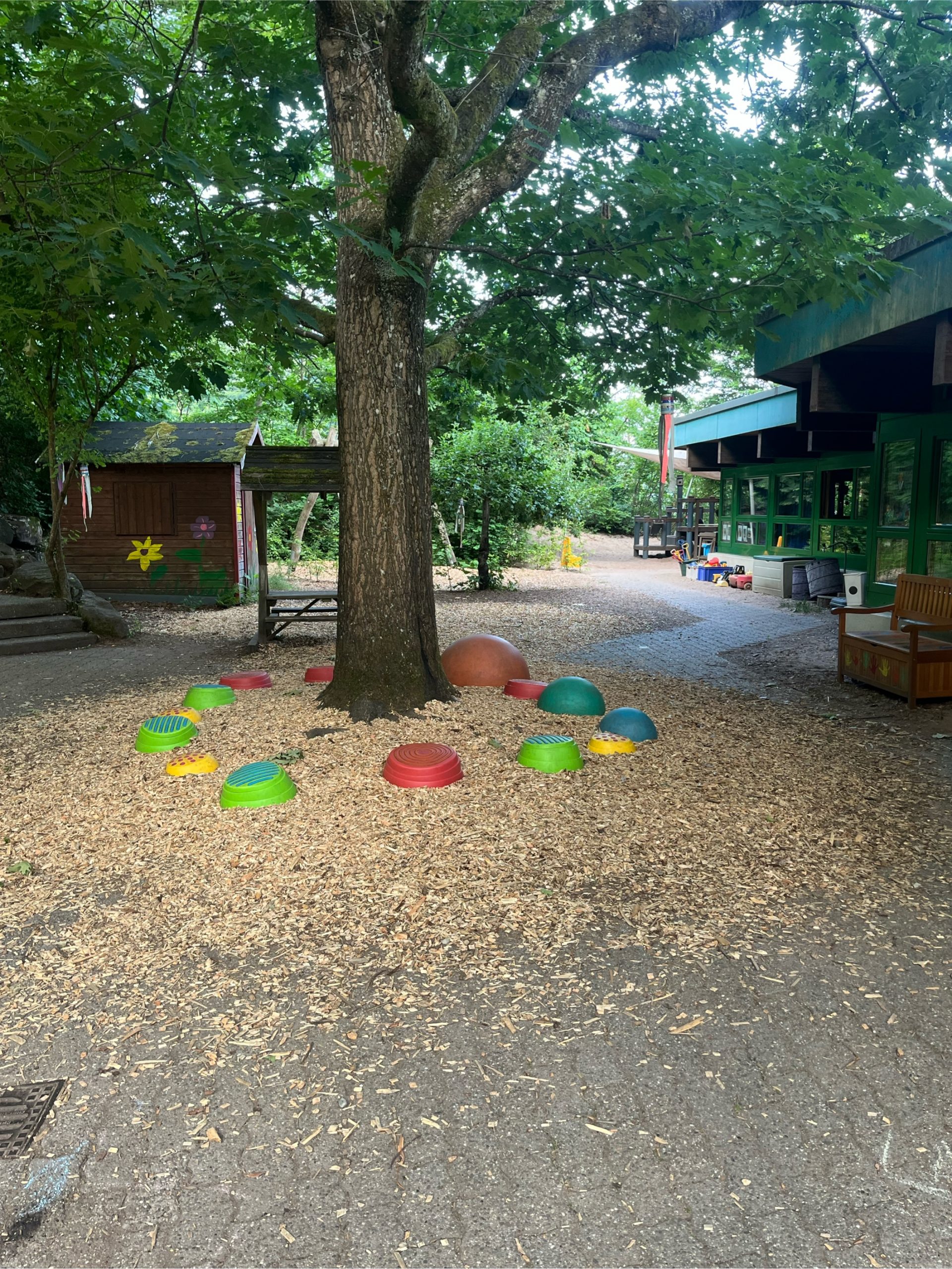 Ein Teil unseres Außengeländes. Zusehen ist unsere große Eiche, Flusssteine zum balancieren und im Hintergrunde unser Gartenhäuschen und ein Teil des Sandkastens.
